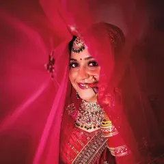 An artistic bridal portrait taken through a flowing red dupatta. This creative technique adds a layer of softness and mystique to the photo.