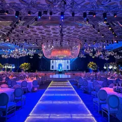 A grand entrance for a glamorous reception. This illuminated walkway, set under a ceiling of modern chandeliers, leads guests towards a stage of contemporary elegance, setting the tone for a spectacular night.