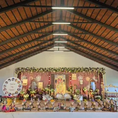 A wide-angle view of a traditional naming ceremony (Namakarna) I decorated. The setup includes a custom backdrop with a deity portrait, a silver cradle for the baby, and an extensive arrangement of silver cow props holding offerings, all under a high, wood-beamed ceiling.