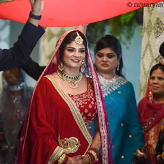 The grand bridal entry is a moment filled with tradition and emotion. Here, the bride makes her way to the ceremony, her serene expression captured under the traditional red fabric held by her family.