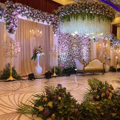A vision of modern romance, this reception stage combines a massive floral wall, a cascading ceiling of white wisteria, and elegant lounge seating. We design spaces that feel both grand and intimately personal.
