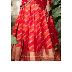 The rich texture and pattern of the orange-red brocade lehenga skirt, featuring a traditional border that grounds the design in heritage.