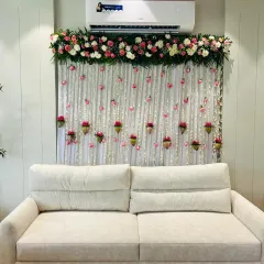 For an elegant and subtle look, we created this backdrop using a white curtain and strings of tuberoses (rajnigandha). Small pots with pink flowers were hung to add a touch of color, perfect for an anniversary or intimate party.