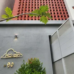 The custom nameplate for "Kadambini" reflects the home's simple yet elegant design ethos. The brick facade provides a textured backdrop, creating a warm and welcoming entrance.