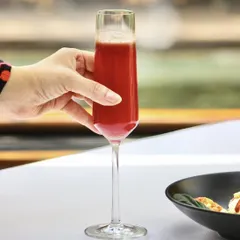 A guest enjoys one of our vibrant cocktails at a table overlooking the water. This image captures the essence of the Indian Accent experience, where every detail, from the drink in your glass to the view, comes together beautifully.
