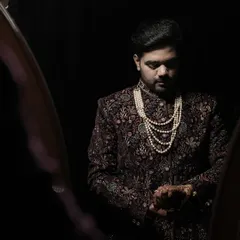 A classic portrait of the groom in a beautifully embroidered sherwani and pearl necklace, checking his watch as he prepares for the ceremony.