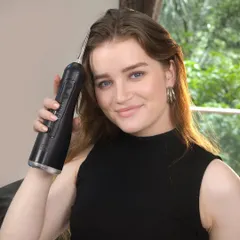 A close-up of a model holding a black water flosser. The focus on the user's happy expression helps to sell the benefits of the product, not just its features.