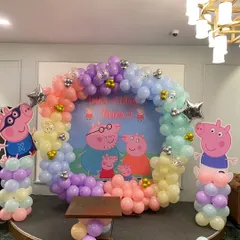 A fun and colorful Peppa Pig themed birthday party. The setup includes a circular balloon arch in pastel rainbow colors and cutouts of the entire Peppa Pig family.