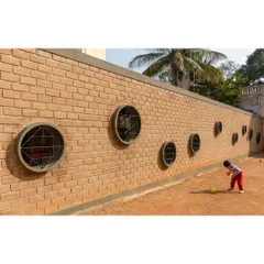 A toddler interacts with the circular windows along a boundary wall at Buddhi School. We use simple, playful architectural details like these to engage children's curiosity and create a stimulating environment.