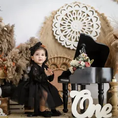 A sweet portrait of the birthday girl in a beautiful black lace dress, ready for her first birthday celebration. The warm, earthy tones of the boho decor create a lovely contrast.