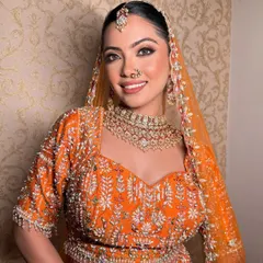 A happy bride glowing in her orange lehenga. The makeup is radiant and fresh, letting her joyful smile be the centerpiece.