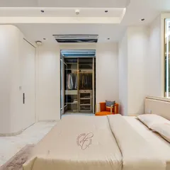 A view from the side of the bed, highlighting the seamless integration of the walk-in closet. The curved wall and minimalist design contribute to the room's open and airy feel.