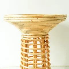 A side view of our hourglass-shaped rattan stool. The intricate, spiraling weave of the base contrasts with the tightly coiled top, making it a sculptural accent piece.