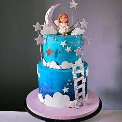 A dreamy, two-tiered cake with a "climb to the moon" theme. It features a blue ombre night sky, edible stars and clouds, a silver ladder, and a charming, hand-sculpted girl figurine sitting on a crescent moon.