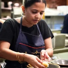 A portrait of a female chef carefully assembling a dish. We believe in celebrating the diverse talent in the culinary world, and this shot captures her skill and concentration in the heart of the kitchen.