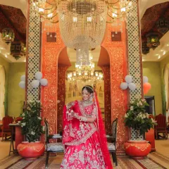 A full-length bridal portrait of Devanshi under a spectacular chandelier. The symmetrical composition and grand setting create a look of pure royalty and elegance for her wedding day.