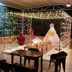 A cozy and royal-themed terrace decoration. This setup features a canopy of fairy lights, a small tent, and low seating, creating a magical and intimate space for a small gathering.