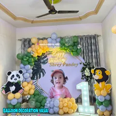 A gentle jungle theme for a first birthday. The setup includes a custom photo backdrop, cute panda and lion cutouts, and a balloon arch in green, yellow, and grey.