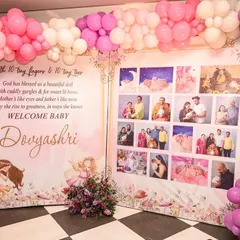 A personalized photo wall surrounded by a pink and purple balloon arch. This display shares the family's journey and welcomes the new baby with a heartfelt poem.