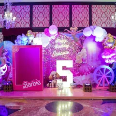 A glamorous Barbie-themed stage with a sparkling pink backdrop, a life-sized Barbie box for photos, and elegant lighting for a chic and stylish party.