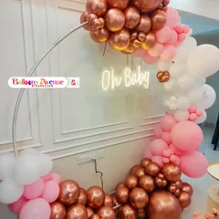 A close-up of a baby shower balloon arch in rose gold, pink, and white, with an 'Oh Baby' neon sign.