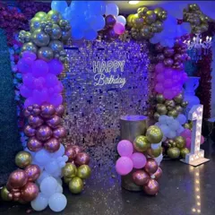 For a glamorous first birthday, I can create a stunning photo corner with a silver shimmer wall. This setup is framed by balloon columns in purple, pink, and metallic tones, and includes a 'Happy Birthday' neon sign and a light-up number '1'.