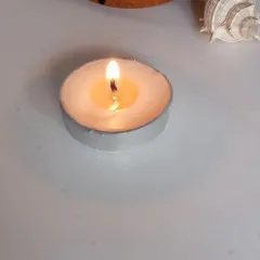 A single, lit tealight on a clean white surface. Sometimes the simplest things are the most beautiful, creating a peaceful retreat with just a small flame.