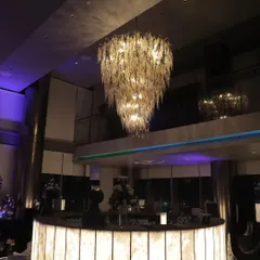 A magnificent, multi-tiered leaf-motif chandelier serves as a stunning centerpiece over the bar at a modern cocktail party, adding a touch of unique artistry to the space.