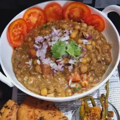 A full bowl of my homemade Matra, garnished with fresh tomatoes, onions, and coriander. It's a wholesome and tangy chickpea curry that is both light and satisfying.