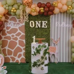 A rustic woodland-themed first birthday with a light-up "ONE" sign against a greenery panel. The decor uses earthy balloon colors and a giraffe-print backdrop for a charming effect.