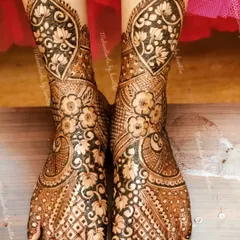 This full-coverage bridal feet mehendi is rich with detail. It features floral and lotus motifs on the ankles and a dense pattern of flowers and checks covering the feet.