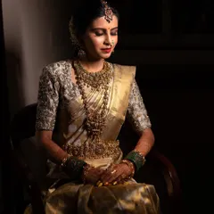 A moment of quiet contemplation for the bride. The dramatic lighting sculpts her features and highlights the incredible detail of her golden saree and temple jewelry.