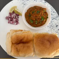 A classic plate of Pav Bhaji, served with soft, buttery pav buns, chopped onions, and a slice of lemon. Our bhaji is a rich medley of mashed vegetables cooked in aromatic spices.