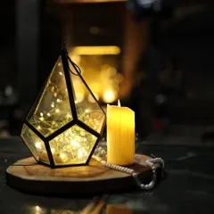 A simple yet beautiful centerpiece detail. A geometric lantern filled with fairy lights and baby's breath, placed next to a candle, adds a touch of magic and warmth to the table.