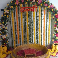 A traditional Haldi ceremony backdrop with a dense curtain of yellow and orange marigold strings. The floral arch and decorative matkas on the sides complete this classic look.