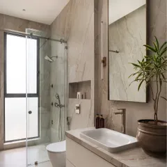 A serene and modern sanctuary. This bathroom features floor-to-ceiling marble-look tiles, a minimalist vanity, and a glass-enclosed shower. A potted plant adds a touch of organic warmth to the clean, bright space.