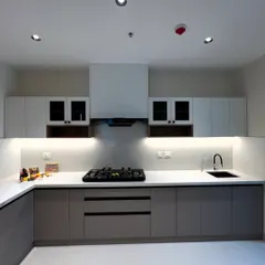 A full view of this minimalist kitchen. It features handleless cabinets in grey and white, frosted glass upper cabinets, and a clean white countertop with an integrated hob and sink.