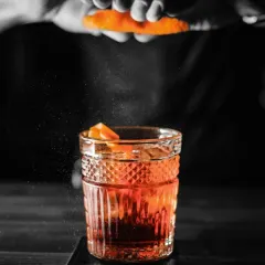 The final touch. A bartender adds a spritz of orange peel to a classic cocktail, releasing aromatic oils that elevate the drink.