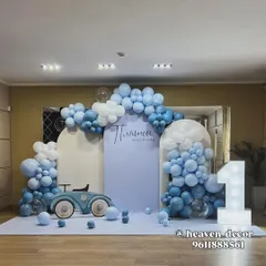 A stylish and modern car-themed first birthday in soft blue and white. The setup includes a vintage car prop, a large light-up number '1', and a beautiful balloon cloud arrangement over arched backdrops.