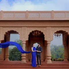 A breathtaking wide shot at a palace, with the blue of the flowing dress creating a stunning contrast against the warm stone architecture. This is a perfect example of a cinematic pre-wedding photo.