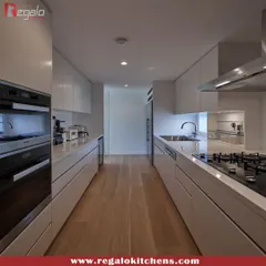 An ultra-minimalist parallel kitchen in all-white. The handle-less design and integrated appliances create a seamless and clean look, making the narrow space feel larger and brighter. The wooden floor adds a touch of warmth.