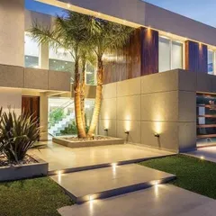 Smart landscape and exterior lighting can transform a home's entrance. Here, uplighting on the palm trees and facade walls creates a dramatic and welcoming approach, highlighting the modern architecture and biophilic elements.