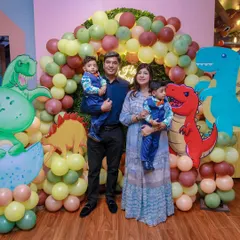 A family poses in front of a dino-rrific birthday setup. We use a mix of friendly dinosaur cutouts and an earthy-toned balloon arch to create a prehistoric world of fun.