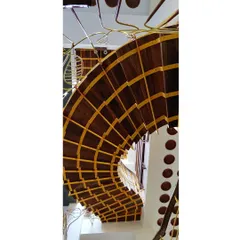 An upside-down view of a staircase reveals its intricate construction. The warm wood of the steps is complemented by the yellow-painted metal framework, showcasing how different composite materials can create a visually striking structure.