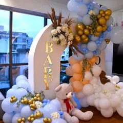 Welcoming a new baby with a grand balloon and floral installation. This double arch in pastel blue, peach, and gold is adorned with fresh flowers and a cute teddy bear.