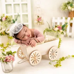 Dressed in soft pink, this baby girl sleeps peacefully in a charming little wooden cart. The surrounding floral arrangement adds a touch of garden magic to this newborn posing idea.
