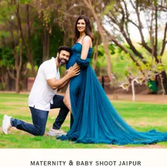 A classic and beloved maternity pose. The partner kneels to kiss the baby bump in a lush green park, a timeless expression of love and excitement for their coming child.