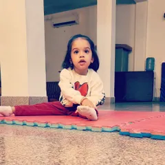 Even our tiniest gymnasts learn foundational poses. This little one is practicing a seated split stretch, an important step in developing the flexibility required for more advanced gymnastics skills later on.