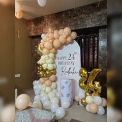 A beautiful and understated decor for Radhika's 24th birthday. This setup includes a white arch backdrop with personalized text, framed by a balloon garland in soft neutral and gold tones.
