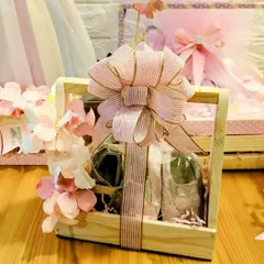 A detail shot of a wooden crate hamper created for a baby girl's arrival. The large, striped bow and floral accents add a touch of sweetness to the curated gifts inside.
